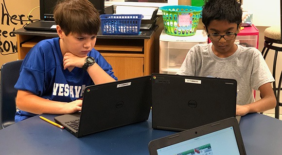 School kids share a desk working on laptops